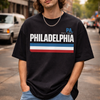 Person wearing a black 'Philadelphia' t-shirt on a city street.