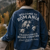 Person wearing a blue jacket with a bear graphic and text on a wooden balcony with a scenic view.