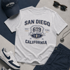 White t-shirt with 'San Diego, California' design, navy cap, sunglasses, and sneakers on a gray surface.