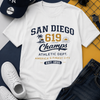 White t-shirt with 'San Diego 619 Champs' design, surrounded by a cap, sunglasses, shoes, and jeans on a multicolored background.