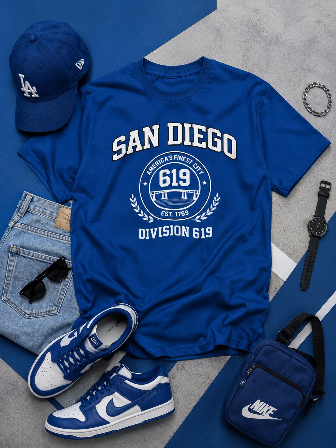 Blue t-shirt with 'San Diego' text, cap, sneakers, and accessories on a gray surface
