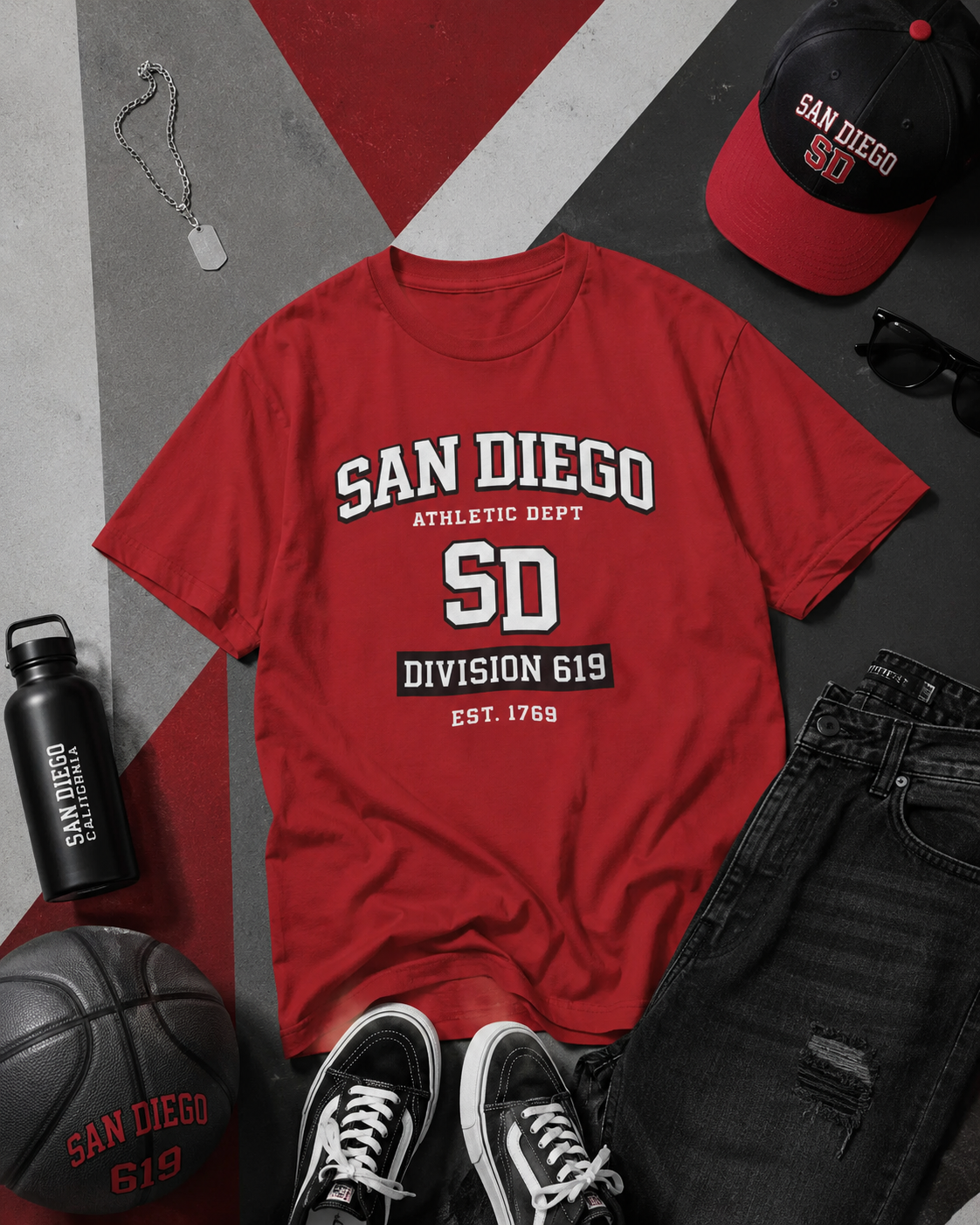 Red t-shirt with 'San Diego Athletic Dept' print, surrounded by accessories on a gray and red background.