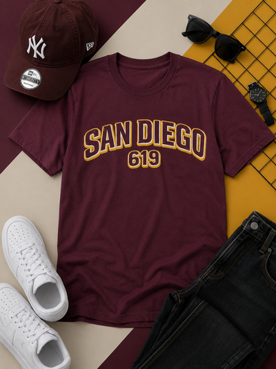 Maroon t-shirt with 'San Diego 619' text, white sneakers, black pants, sunglasses, and a cap on a patterned surface.