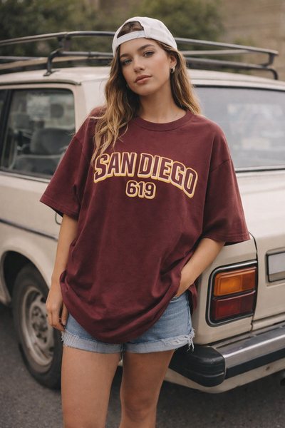 Woman wearing a 'San Diego 619' t-shirt standing next to a vintage car.