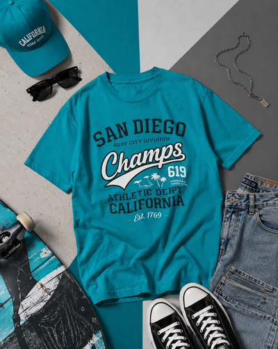 Turquoise t-shirt with 'San Diego Champs' text, surrounded by a cap, sunglasses, jeans, and sneakers on a gray surface.