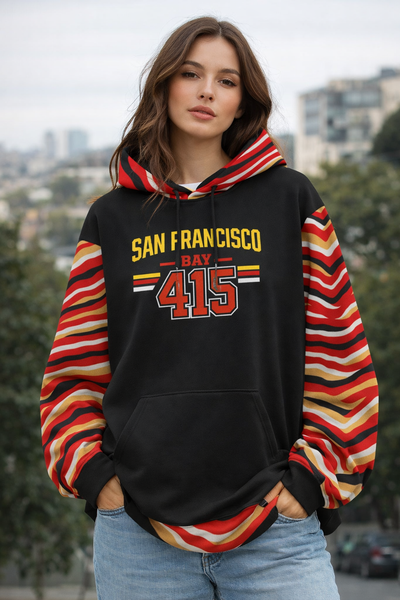 Woman wearing a black hoodie with colorful sleeves and 'San Francisco Bay 415' text, standing outdoors.