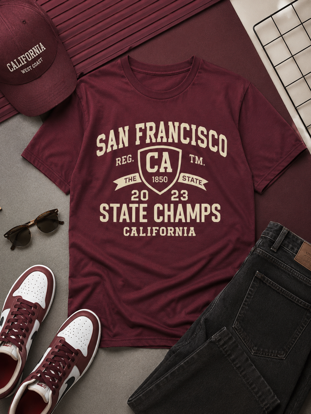 Maroon t-shirt with 'San Francisco State Champs' text, maroon cap, white sneakers, sunglasses, and black pants on a gray surface.