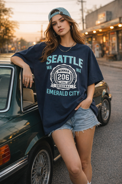 Woman wearing a 'Seattle' t-shirt leaning against a vintage car on a street.