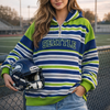 Person wearing a striped hoodie with 'Seattle' text, holding a helmet on a sports field.