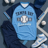 Baseball-themed outfit with blue and navy shirt, shorts, shoes, and cap on a gray surface.