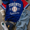 Blue and red 'Toronto Baseball Academy' t-shirt with accessories on a gray surface
