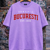 Purple t-shirt with 'ROMANIA BUCURESTI EST. 1459' text on a hanger against a graffiti-covered wall.