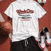 White t-shirt with 'Windy City Basketball' design, black shorts, sneakers, basketball, and headphones on a red sports court.